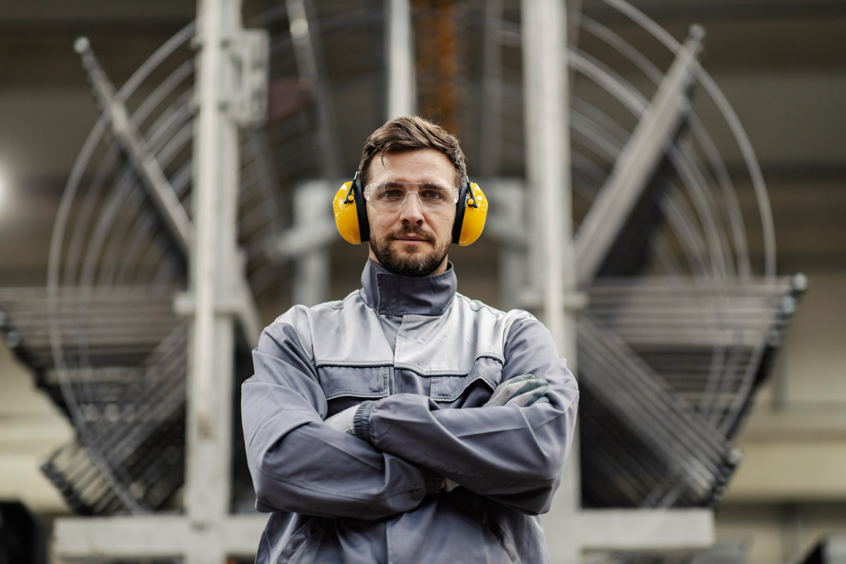 A heavy industry worker with arms crossed makes eye contact whil